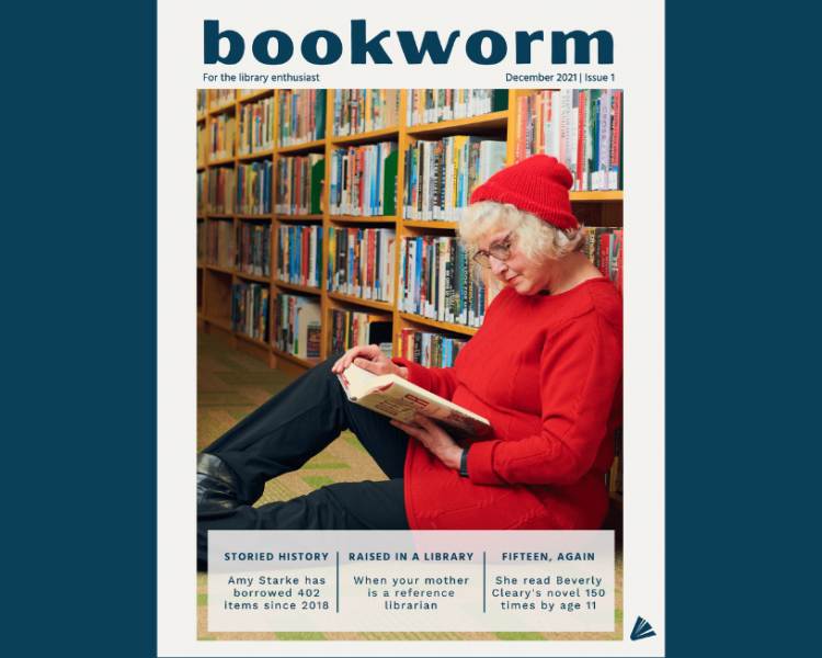 Woman wearing black pants, red shirt and glasses sitting and reading against a bookshelf.