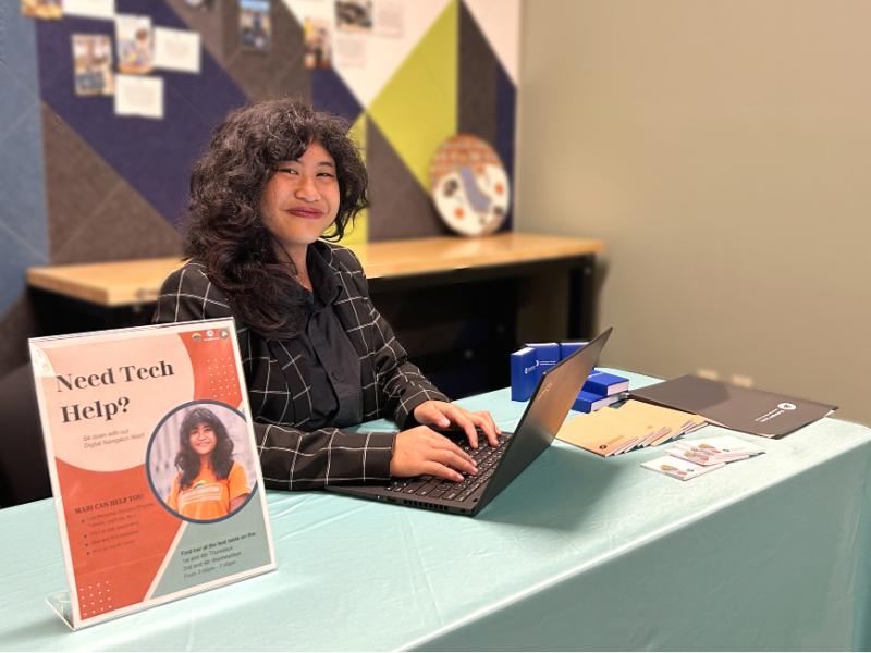 Mari sits at her booth on her laptop ready to help.