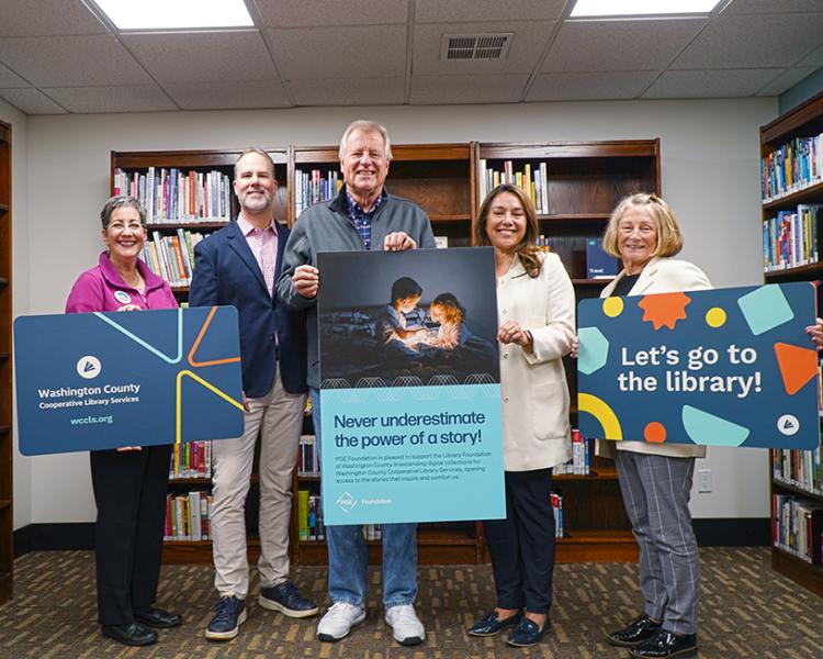 Members of the community hold up giant library cards and pose with their check at West Slope Library.