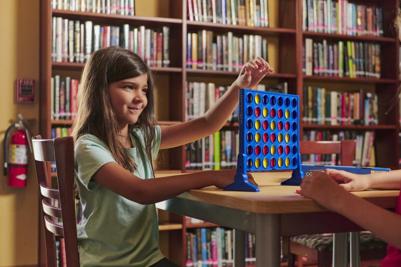 Young girl plays connect four in the library.