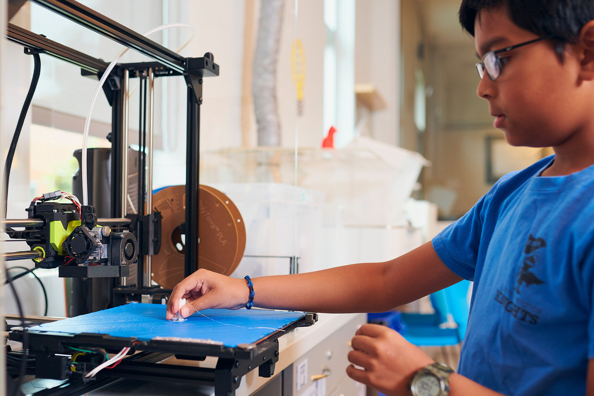 Boy in glasses works with machine in a maker lab space