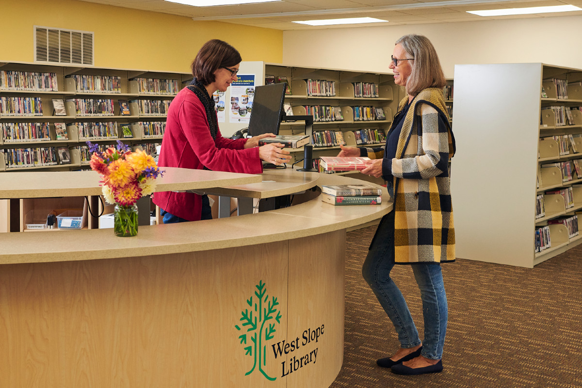 Library staff receives books from patron at round desk